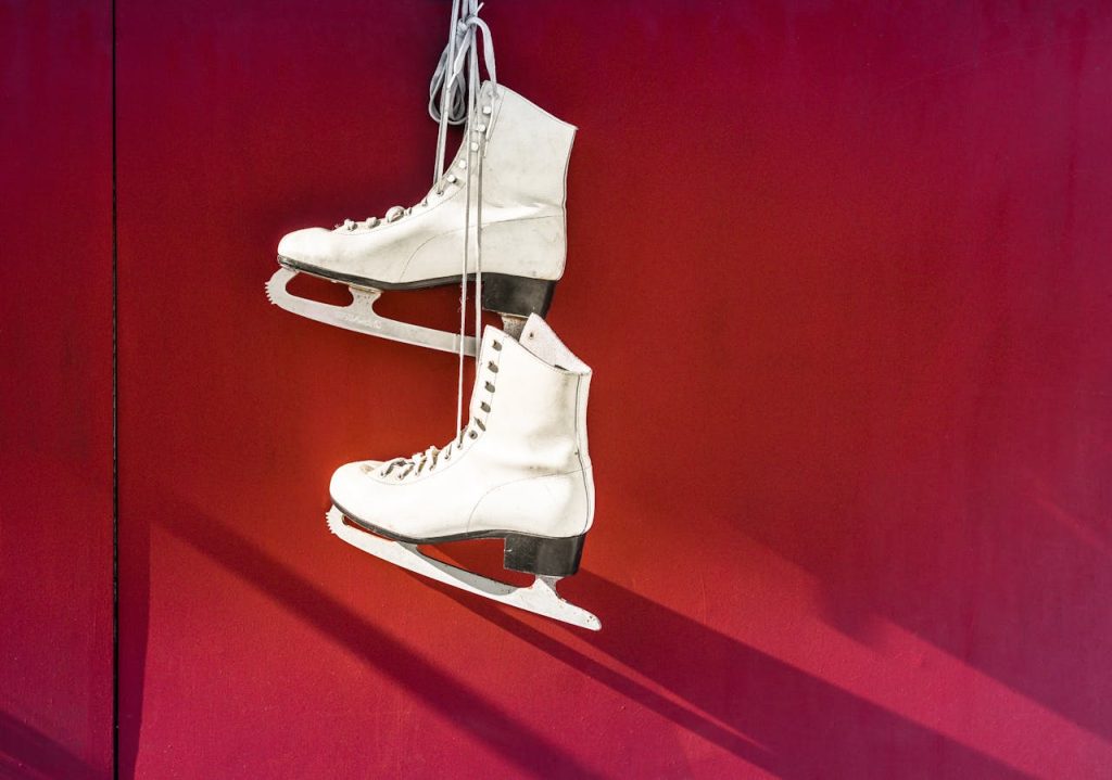 Pair of white ice skates hanging on a vibrant red wall, perfect for winter sports imagery.